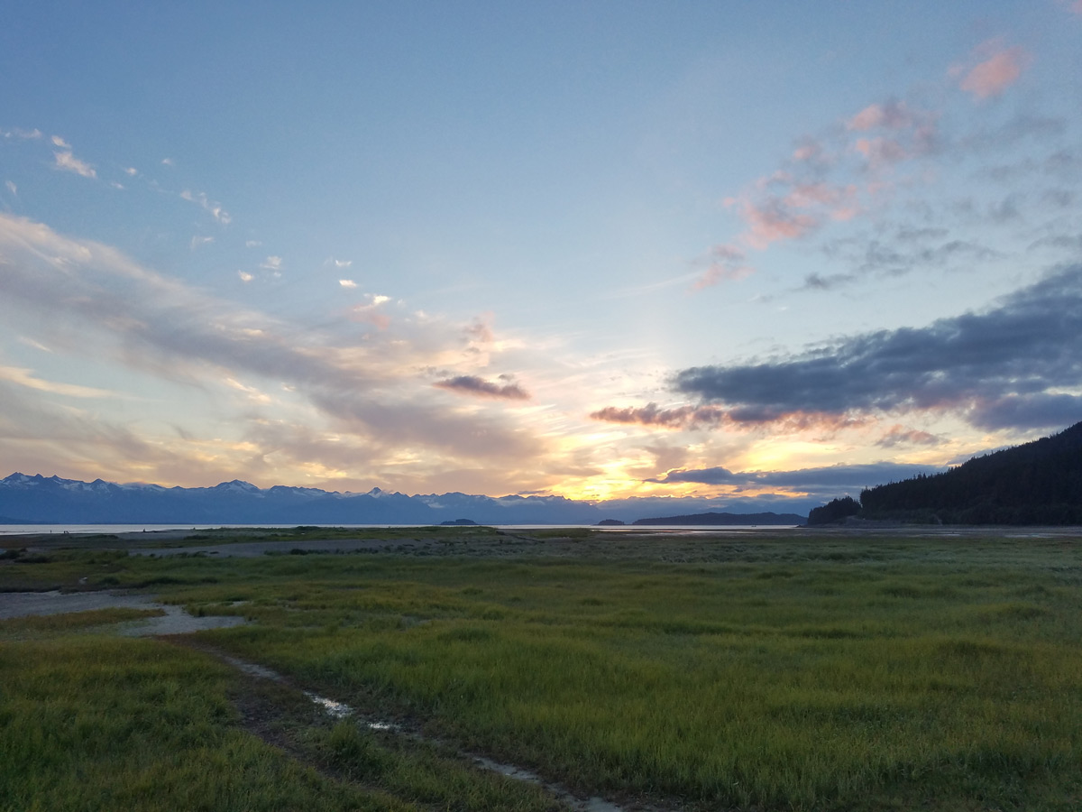 A sscenic landscape shot of a field in Juneau Alaska with the sun setting behind the clouds